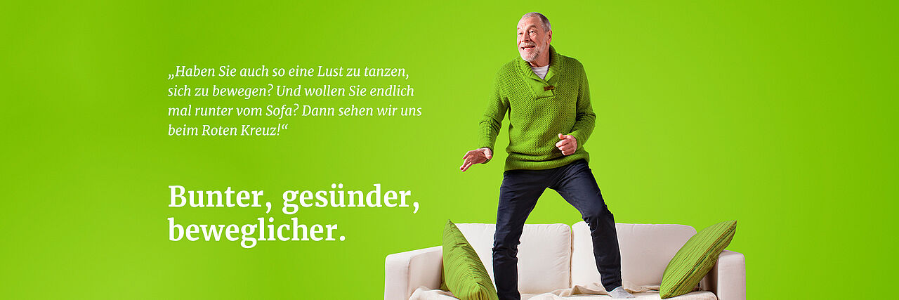 Aktivierender Hausbesuchsdienst Älterer Mann mit grünem Pullover bewegt such auf einem Sofa.